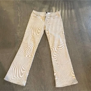 Beige och vita mönstrade byxor - Säljer ett par snygga beige och vita zebramönstrade byxor i bra skick. De har en bootcut-stil och är lågmidjade, vilket ger en skön passform. Perfekta för både vardag och fest! 🦓✨midjemått ca39 cm innerbenslängd 77 cm raktöver