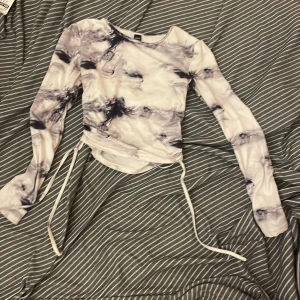 Mönstrad långärmad topp från Shein - Säljer en cool långärmad topp från Shein i svartvitt mönster. Toppen har snörning i sidorna för en justerbar passform och är tillverkad i ett mjukt syntetmaterial. Perfekt för en trendig look!