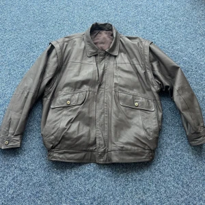 Brun Vintage skinnjacka - Säljer en klassisk brun vintage skinnjacka med dragkedja och knappar. Jackan har långa ärmar och två stora fickor framtill med knappstängning. Perfekt för en stilren look. Avtagbara armar.                                                TVÅ DEFEKTER —En defekt är dragkedjan då den delar sig ibland när den dras upp. En annan är den knappen som jag tog bild på vid dragkedjan som sitter lite löst av sig men är fortfarande fullt intakt. 