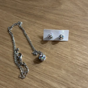 Glittrigt smyckesset i silver - Snyggt set med halsband, örhängen och justerbar ring i silver! Smyckena har glittrande stenar som fångar ljuset fint. Oanvända! 