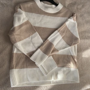 Randig tröja från H&M Divided - Säljer en snygg randig tröja från H&M Divided i beige och vit. Tröjan har långa ärmar och en rund halsringning. Perfekt för en avslappnad stil. Bild 1:framsida Bild 2:Baksida Bild 3: Framsida Bild 4: Märke och storlek Bild 5:Detalj Skick: Tröjan är använd men i ett bra skick 