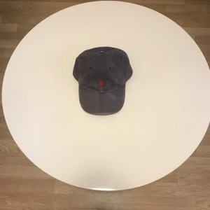 Blå keps från Polo Ralph Lauren - Snygg blå keps från Polo Ralph Lauren med röd broderad logga framtill. Justerbar rem baktill för perfekt passform. Perfekt för en avslappnad stil. Lite sol blekt