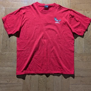 Röd t-shirt från No Fear - Cool röd t-shirt från No Fear med tryck av ögon och texten 'Fear is in the eye of the beholder' på baksidan. Framsidan har en mindre logga med ögonmotiv. Perfekt för en avslappnad stil. 100% bomull