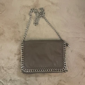 Grå Tiamo Väska  - Hej! Säljer denna superfina gråa axelremsväskan/handväskan från märket Tiamo. Anledningen till att jag säljer är den är pga att den helt enkelt inte kommer till användning längre. Den har små slitningar på baksidan av väskan (sista bilden) men annars är den i fint skick. Hör mer än gärna av dig om du skulle ha några frågor!