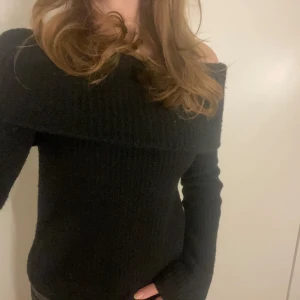 Svart offshoulder stickad tröja - Säljer en stilren svart offshoulder stickad tröja. Perfekt för en trendig look med sin åtsittande passform och långa ärmar. Enkelt att matcha med olika outfits för en chic stil.
