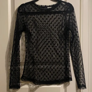 Svart transparent topp med prickar!  - Snygg svart transparent topp med prickigt mönster. Den har långa ärmar och är perfekt för en trendig look. Passar bra att bära över ett linne eller en bralette för en stilren outfit.