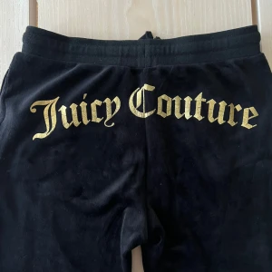Svarta velourbyxor från Juicy Couture - Snygga svarta velourbyxor från Juicy Couture med guldtryck. Byxorna har en bekväm passform med snörning i midjan och Juicy-logga på framsidan. Perfekta för skolan eller mys hemma!! Mycket bra pris pågrund av dess skick.