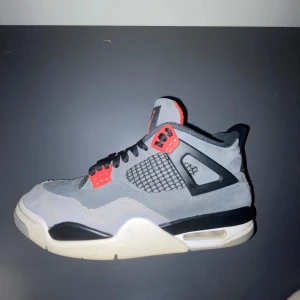 Jordan 4 bred - Snygga Nike Air Jordans i grått och svart med röda detaljer. Skorna har en klassisk design med snörning och en synlig luftdämpning i sulan. Perfekta för dig som vill ha en stilren och sportig look.