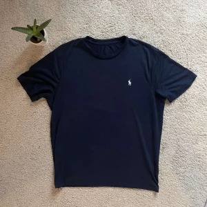 Mörkblå t-shirt från Ralph Lauren - Snygg svart t-shirt från Ralph Lauren med en liten broderad logga på bröstet. Perfekt för en stilren look. Kortärmad och tillverkad i mjukt material för extra komfort.