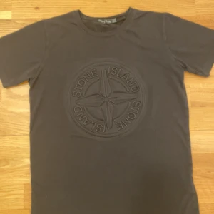 Svart t-shirt från Stone Island - Snygg svart t-shirt från Stone Island med ett stort, upphöjt logotypmotiv på framsidan. Perfekt för en stilren och modern look. Kortärmad design som passar bra till vardags.