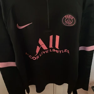 Svart/Rosa fotbollströja från Nike/ PSG - Snygg svart fotbollströja från Nike med rosa detaljer och PSG-logga.  Tröjan är i ny skick. Helt äkta.  Etiketten finns med.