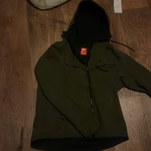 Olivgrön hoodie från Nike - Säljer en olivgrön hoodie från Nike med svart huva och dragkedja. Perfekt för en avslappnad stil. Den har en diskret Nike-logga på bröstet och är tillverkad i ett mjukt material, pris kan diskuteras vid Dm! Snabb afär!