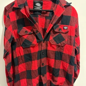 skjorta - Snygg röd och svart rutig skjorta från Dickies i storlek X Small. Skjortan har långa ärmar och knappar framtill samt två bröstfickor med knappstängning. Perfekt för en avslappnad stil.
