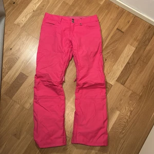 Rosa skidbyxor från Burton - Snygga rosa täckbyxor från Burton, perfekta för vinterns äventyr. Tillverkade i ett slitstarkt syntetmaterial med DRYRIDE-teknologi.