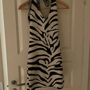 Zebramönstrad klänning med knytband - Snygg zebramönstrad klänning med v-ringning och knytband i nacken. Perfekt för en djärv look. Klänningen har en hyfsat tajt passform och är ärmlös, vilket gör den bekväm.