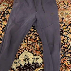 Nike byxor - Säljer ett par mörkblå mjukisbyxor från Nike med snörning i midjan och dragkedjefickor. Perfekta för en avslappnad stil.