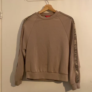 Beige sweatshirt från Guess - Säljer en beige sweatshirt från Guess med logotyp längs ärmarna. Tröjan har en rund halsringning och långa ärmar. Perfekt för en avslappnad stil. Hör av dig vid intresse! Orginal priset är runt 1100, jag hade velat ha 700 för den. Priset är såklart förhandlingsbart vid snabb affär💞