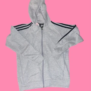 Grå hoodie från Adidas - Säljer en grå hoodie från Adidas med dragkedja och svarta ränder längs ärmarna. Storlek 11 - 12 år går på min vän som är STl XXS 