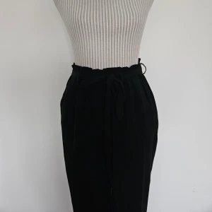 Svarta byxor med knytband i midjan från BikBok - Svarta byxor med hög midja och band i midjan. Byxorna är i en rak modell med smala ben. Använda en del så spår av användning finns. Lite noppriga. Storlek S.