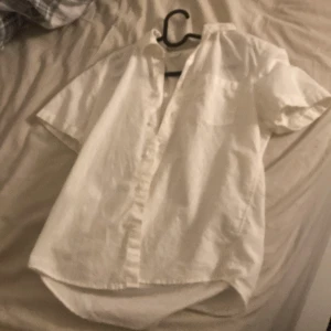 Vit kortärmad skjorta från Lindex - Säljer en stilren vit kortärmad skjorta från Lindex. Perfekt för varma dagar med sin lätta och luftiga design. Skjortan har knappar framtill och en klassisk krage. Passar utmärkt för både avslappnade och mer uppklädda tillfällen. Den är också linne, använt på midsommar annars aldrig 