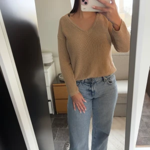 Beige stickad tröja från NAKD - Säljer en snygg beige stickad tröja från NAKD. Tröjan har en v-ringad design och långa ärmar, perfekt för kyligare dagar. Den är i en mjuk och bekväm stickad kvalitet som passar till många olika outfits.