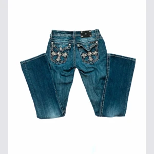 Bootcut jeans - Lågmidjade bootcut miss me jeans med blomdetaljer på fickorna. Midjemått tvärs över är 37 cm och innerbenslängden 85 cm. Lite slitna vid benslutet och saknar en av knapparna på fickorna, i övrigt fint skick. Använd köp nu!💞