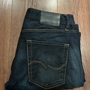 Mörkblå jeans från Jack & Jones - Snygga mörkblå jeans från Jack & Jones med klassisk femficksdesign och kontrastsömmar. Jeansen har en straight passform och är tillverkade i slitstarkt denim. Perfekta för en avslappnad stil. Storlek: W32L32. I mycket bra skick!