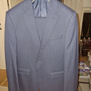 Kostym från Brothers - Snygg randig kostym från Riley i en stilren mörkblå färg. Kostymen har en slim fit passform och är tillverkad i en blandning av ull och polyester. Perfekt för formella tillfällen med sin klassiska kavaj och matchande byxor. Plaggen är endast använda en gång.