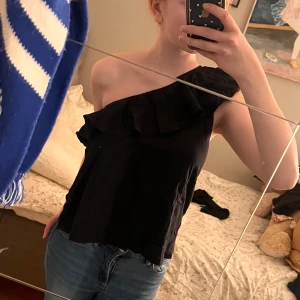 Svart one-shoulder topp - Säljer en svart one-shoulder topp med volang. Volangen sträcker sig runt hela toppen. 