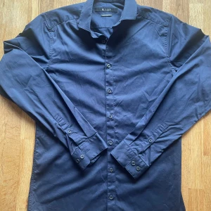 Mörkblå skjorta från Tiger of Sweden - Snygg mörkblå skjorta från Tiger of Sweden i slim fit. Skjortan har långa ärmar och knappar framtill. Perfekt för en stilren look. Storlek: 38 Hör av dig vid några frågor.😊
