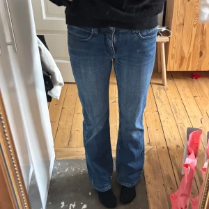 Lågmidjade utsvängda jeans - Blåa utsvängda lågmidjade jeans. Midjemått 37cm och passar mig som är 175cm lång. Lite slitningar längst ner på byxkanten
