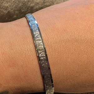 Silverfärgat armband med mönster - Elegant silverfärgat armband med ett subtilt mönster. Armbandet har en smidig låsning och en stilren design som passar perfekt för att ge en extra touch till din outfit.