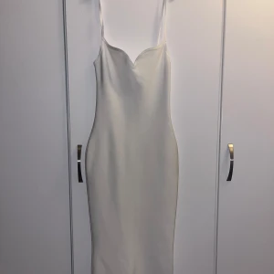 vit klänning - Elegant vit klänning med smala axelband och en figurnära passform. Klänningen har en stilren design med en dragkedja i ryggen för enkel påklädning. Från Babyboofashion, storlek S! 