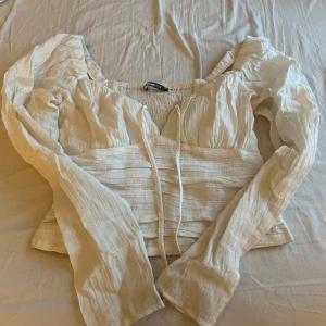 Vit blus från Gina Tricot - Säljer en söt vit blus från Gina Tricot i storlek XS. Blusen har långa ärmar och en knytning framtill. 