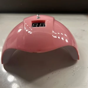 Rosa LED-lampa för naglar - Säljer en rosa LED-lampa för naglar med digital display och timerfunktioner på 30, 60 och 90 sekunder. Lampan har flera LED-lampor inuti och kommer med en vit USB-kabel för strömförsörjning. Perfekt för hemmabruk för att härda gelnaglar. Är från shein , är också öppen för nya erbjudande av priset