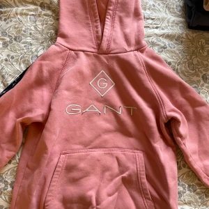 Rosa hoodie från GANT - Säljer en snygg rosa hoodie från GANT med logga på bröstet, däremot sitter bokstäverna lite sämre - utöver det i gott skick! Perfekt för en avslappnad stil.