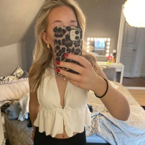 Vit ärmlös topp - Säljer en stilren vit ärmlös topp med volangdetaljer. Toppen har en djup v-ringning och är croppad, vilket ger en trendig look. Perfekt för varma dagar eller sommarens fester.