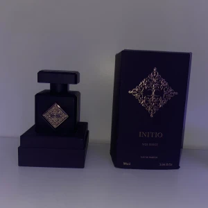 Initio Side Effect Eau de Parfum - Exklusiv parfym från Initio, Side Effect, i en elegant lila flaska med gulddetaljer. Flaskan rymmer 90 ml och har en lyxig design med ett dekorativt mönster på framsidan. Perfekt för den som söker en sofistikerad doftupplevelse.