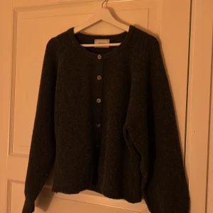 Mörkgrå kofta från Neo Noir - Säljer en stilren mörkgrå kofta från Neo Noir. Den har långa ärmar och knappar framtill, perfekt för kyliga dagar. Koftan är gjord i ett mjukt material som ger en skön känsla. Passar bra till både jeans och kjol. knapparna går inte att knäppas upp