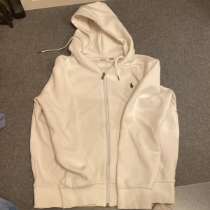 Vit hoodie från Ralph Lauren - Säljer en stilren vit hoodie från Ralph Lauren med dragkedja och huva. Den säljs för att den är för liten användes under 10 gånger. Köptes för 1500kr