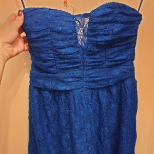 Blå spetsklänning från Jeane Blush - Säljer en NY superfin blå klänning från Jeane Blush i storlek M. Men passar mera S. Klänningen är axelbandslös och har en vacker spetsdesign med en liten öppning framtill. Perfekt för festliga tillfällen! Den har en dragkedja i ryggen.