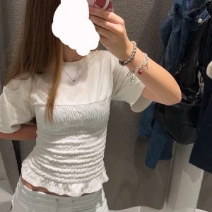 Vit smockad topp - Säljer en superfin vit smockad topp med korta ärmar. Den har en tight passform och är perfekt för både vardag och fest. Toppen är i ett mjukt och bekvämt material. Kan tänka mig att sänka priset ytterligare vid snabb affär.