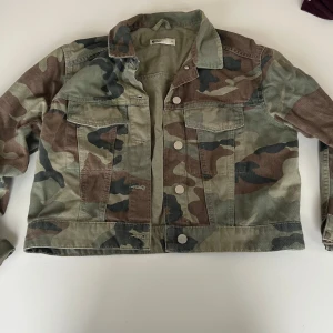 Camouflage jeansjacka - Säljer en cool jeansjacka med camouflage-mönster. Jackan har knappar framtill och två bröstfickor. Perfekt för en avslappnad stil och passar bra till både vår och höst.