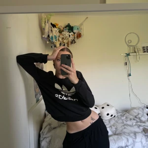 Svart sweatshirt från Adidas - Säljer en svart sweatshirt från Adidas med deras ikoniska vita logga på framsidan. Tröjan är långärmad och gjord i ett mjukt bomullsmaterial, perfekt för en casual look. Den har en normal passform och är i nyskick. Perfekt för höst och vår!