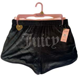 Säljer ett par snygga svarta shorts från Juicy Couture. De är gjorda i ett mjukt och glansigt material som känns lyxigt. Shortsen har en elastisk midja och en cool Juicy-logga i strass på framsidan. 