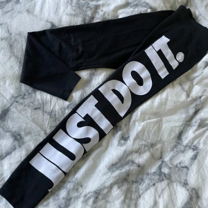 Svarta leggings från Nike - Säljer ett par svarta leggings från Nike med det ikoniska 'Just Do It' trycket i vitt längs benet. Perfekta för träning eller en avslappnad dag. De är i bra skick och superbekväma!