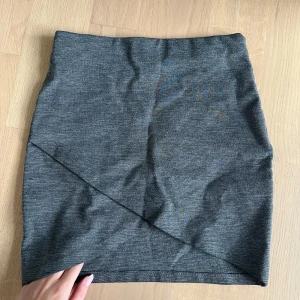 Grå kjol med omlott-detalj  - Grå minikjol med omlott-detalj fram. Resår i midjan och mjukt material. Både snygg och bekväm. 