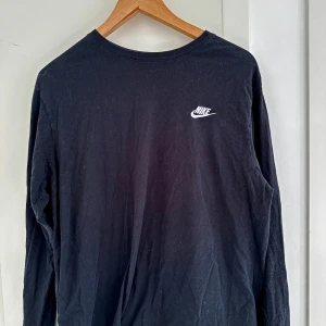 Nike tröja - Nike-tröjan "The Nike Tee" är en klassisk långärmad tröja i svart färg. Den har en enkel och ren design, där den svarta färgen dominerar hela tröjan. Materialet är en blandning av bomull och polyester, vilket ger en mjuk och bekväm känsla. 