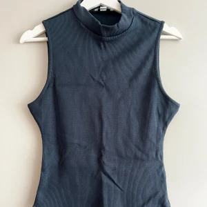 Mörkgrå ribbad polotopp från Topshop - Säljer en snygg mörkgrå ribbad polotopp från Topshop. Den är ärmlös och har en tight passform som är perfekt för både vardag och fest. Tillverkad i ett mjukt och stretchigt material som sitter bekvämt hela dagen.