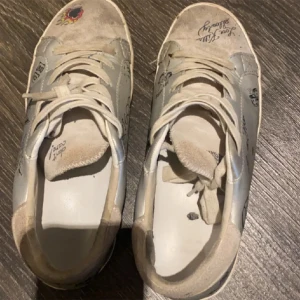 Vita sneakers med unika tryck - Säljer ett par vita sneakers med coola,  tryck och mönster. Skorna har snörning och är i välanvänt skick. Perfekta för dig som vill ha något unikt och personligt i garderoben! slitningar